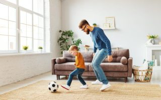 Dad playing soccer with his young son in the living room