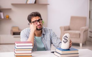Man with his fist on his chin with books on one side and a bag with a dollar sign on the other side