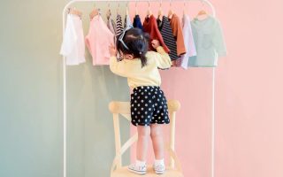 two year old looking through a rack of toddler clothes