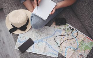 Woman sitting on the floor with a map and hat beside her as she plans a trip.