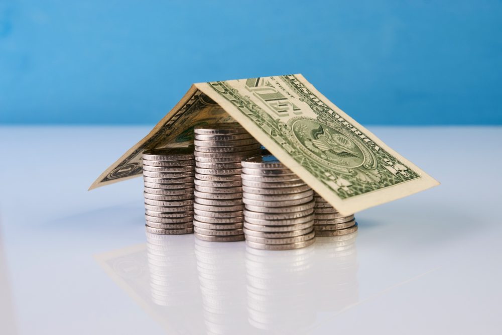 Stacks of coins covered with a folded dollar bill to look like a house.