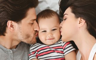 Beloved baby. Parents kissing their cute infant, closeup, panorama
