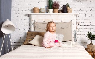 Beautiful girl is sitting on the bed and is holding a toy.