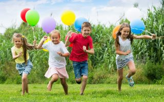 Playful boy and girls running and playing with colorful balloons in garden on green grass