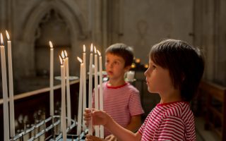 Little boy prays and puts a candle in Orthodox Church, sad kid with faith