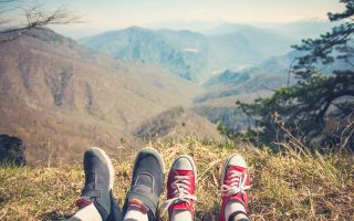 foot girl and guy traveler who sits atop a mountain and looks at a mountain plateau View from back of the tourist traveler on background mountain.