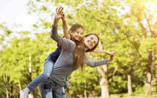 happy mother with her daughter in the park on a sunny day, imitating the flight of the aircraft