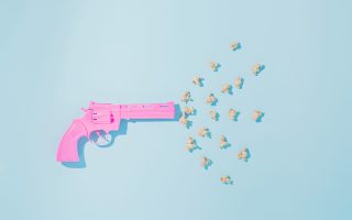 Pink pistol shoots popcorns on pastel blue background. Candy colors. Minimal flat lay concept of non-violence and peaceful conflict resolution.