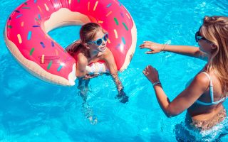 Little girl with her mom having fun in swimming pool.