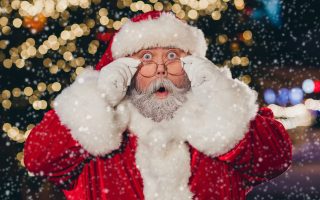 Portrait of impressed santa claus pouted lips arms touch glasses staring cant believe midnight tree garland city center outside.