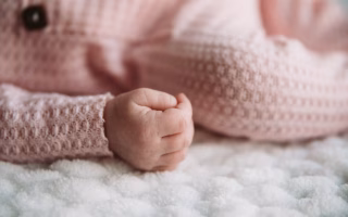 A smiling baby girl lying on a soft blanket, looking up with bright eyes and a joyful expression