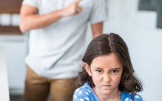 Portrait of angry daughter with arms crossed while father scolding