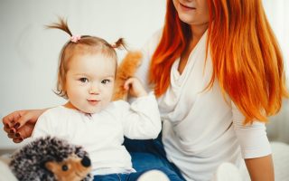 Beatuful ginger mother playing with daughter. Little girl sitting on a bed at home. A young mother clinging to a daughter of hair