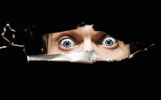 Scary eyes of a man spying through a hole in the wall close up
