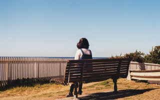 A woman sitting alone by a window, gazing outside with a thoughtful, distant expression