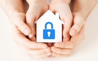 real estate and family home security concept - closeup picture of male and female hands holding white paper house with blue lock