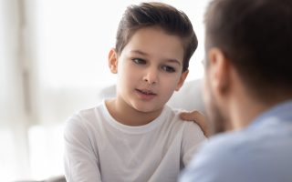 Back view of dad sit on couch with preschooler son talking sharing thoughts or problems, loving father speak have conversation with little boy child, support him showing care and understanding
