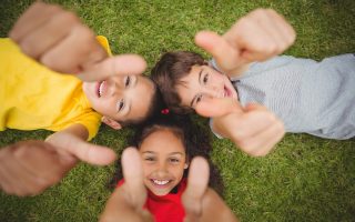 Cute pupils lying on grass smiling on elementary school campus