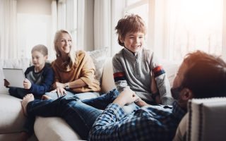 Parents, children and family with playing on sofa, tablet and bonding with love, joke or funny memory in living room. Mother, father and kids with games, app and connection to relax on couch in home.