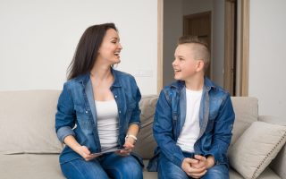 Happy mother and son sitting on sofa and using digital tablet at home