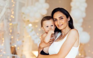 A close-up portrait of a charming mother and her cute boy at home. A smiling attractive woman and her sweet baby in the bedroom. A young mom hugs her son.