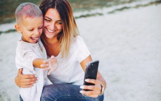 Family sitting on a sand. Mother in a white t-shirt. Cute little boy with paints on his face