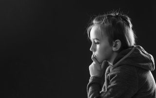 Stressed boy over black background, copy space. Childhood, bulling and family concept. Sad young boy thinking about his problems. Afraid child sitting quiet in dark. Young boy suffering from anxiety.