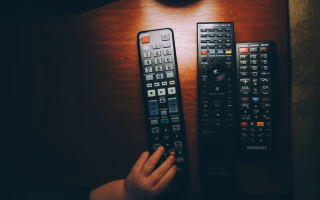 Child's hand reaching for a TV remote on a wooden table.