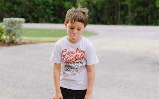 Child sticking out tongue with slouched posture outdoors