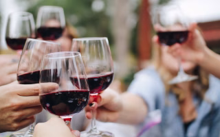 People clinking glasses of red wine together in a celebratory toast.