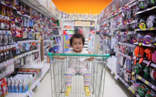 Baby sitting in a shopping cart in a store aisle.