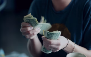 Person counting a stack of dollar bills