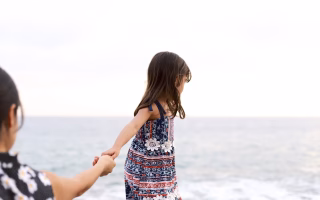 Adult and child holding hands by the ocean.