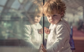 Young child staring out a window with a serious expression.