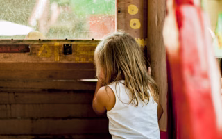 Child peeking through a wooden window indoors.