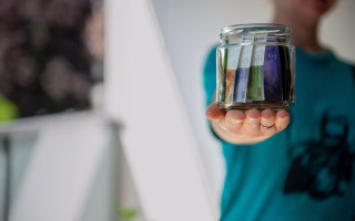 Person holding a jar filled with folded currency bills.