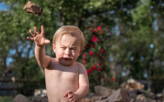 Toddler throwing a rock with a frustrated expression