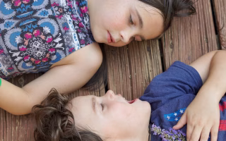 Two young siblings facing each other in a playful but tense moment, with expressive faces showing competition or conflict, while a parent nearby observes with a mix of patience and fatigue—capturing the everyday challenges of managing sibling rivalry.
