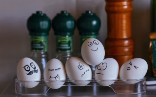 Eggs with funny hand-drawn faces sitting in a clear egg holder.