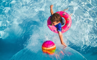Child in a swim ring reaching for a colorful ball in a pool