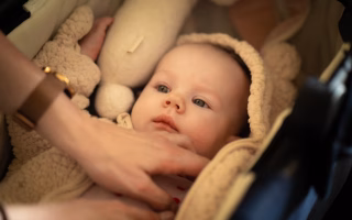 Baby lying in a stroller wearing a soft beige outfit, gently touched by a caregiver.
