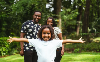 Smiling child with arms outstretched, parents standing behind