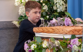 A young child sitting quietly with a soft, pensive expression, wrapped in a cozy blanket, while an adult offers quiet support—illustrating the tender care and thoughtful words needed to comfort a grieving child.