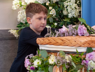 A young child sitting quietly with a soft, pensive expression, wrapped in a cozy blanket, while an adult offers quiet support—illustrating the tender care and thoughtful words needed to comfort a grieving child.