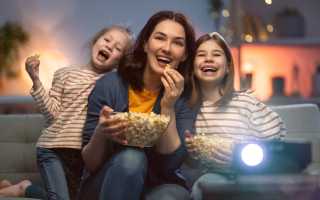 A mother and two children watching TV together, sharing popcorn.