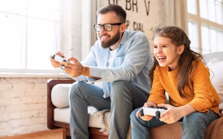 Father and daughter smiling while playing video games together.
