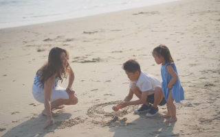 Woman and kids drawing in the sand at the beach.