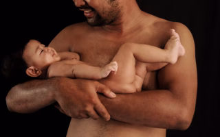 Shirtless father holding and smiling at his baby.