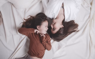 Mother and daughter lying on bed, smiling at each other