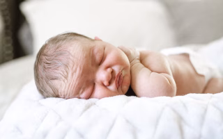 Newborn baby sleeping peacefully on a soft white blanket.